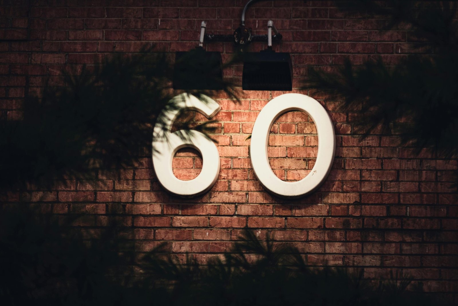 Illuminated number 60 on a brick wall framed by shadows, creating a mysterious atmosphere.